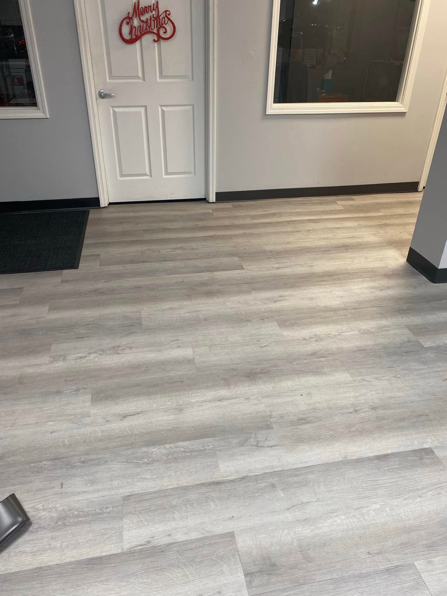 Empty room with light gray wood flooring, white front door, and two small windows.