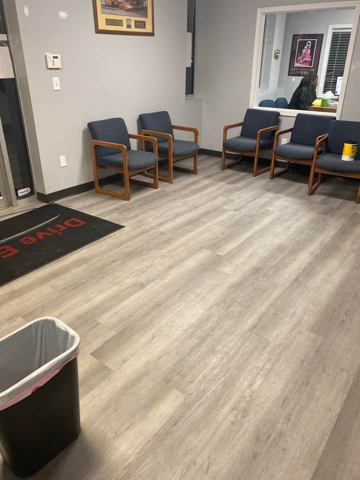 Empty waiting room with blue chairs, light wood floor, and a trash can in the foreground.