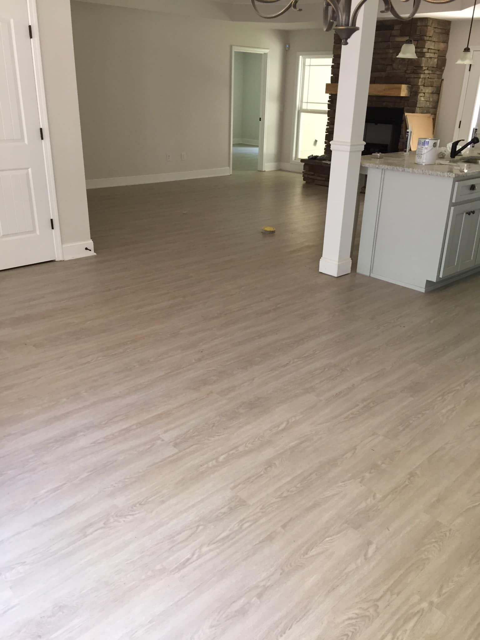 Empty unfurnished room with light wood flooring, white walls, and a small kitchen area on the right.
