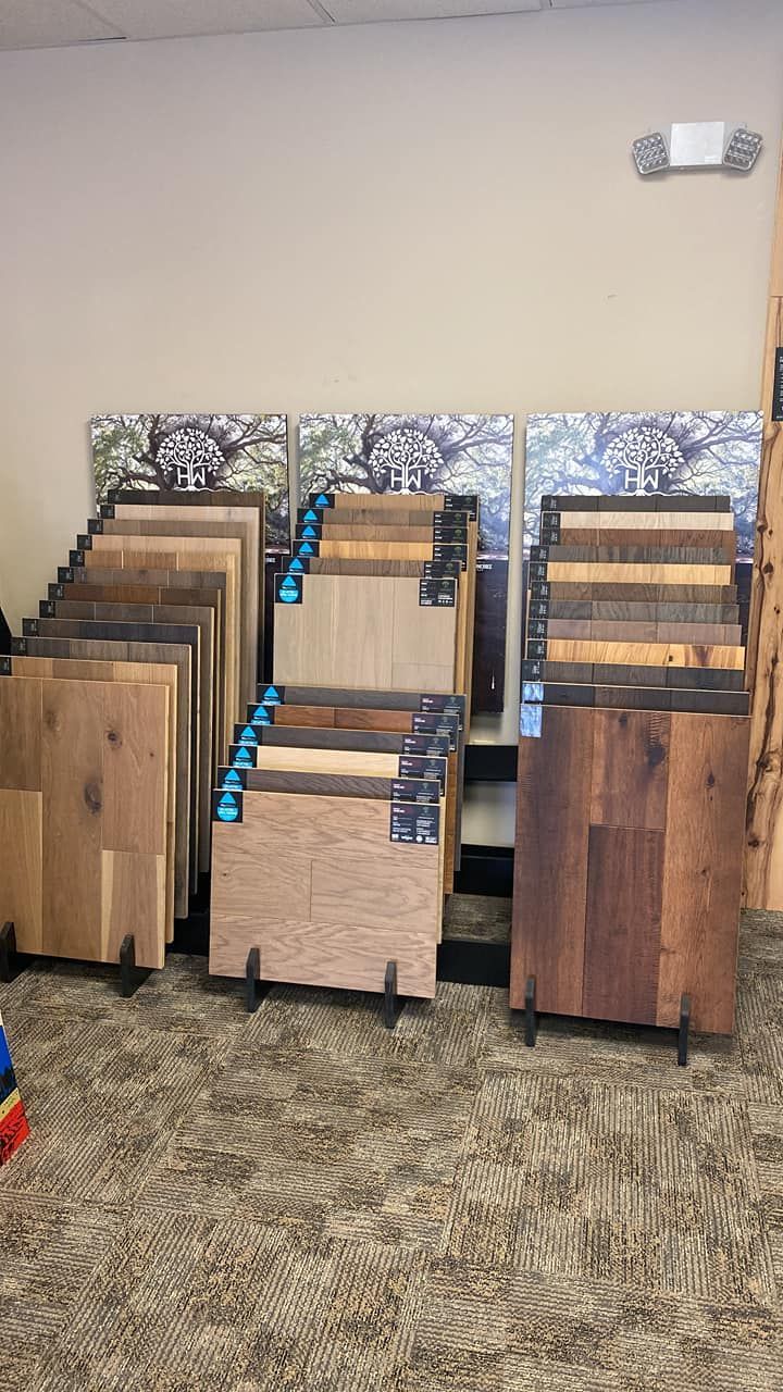 Three wooden folding tables stacked in a carpeted room, with blue straps and a beige wall behind them.