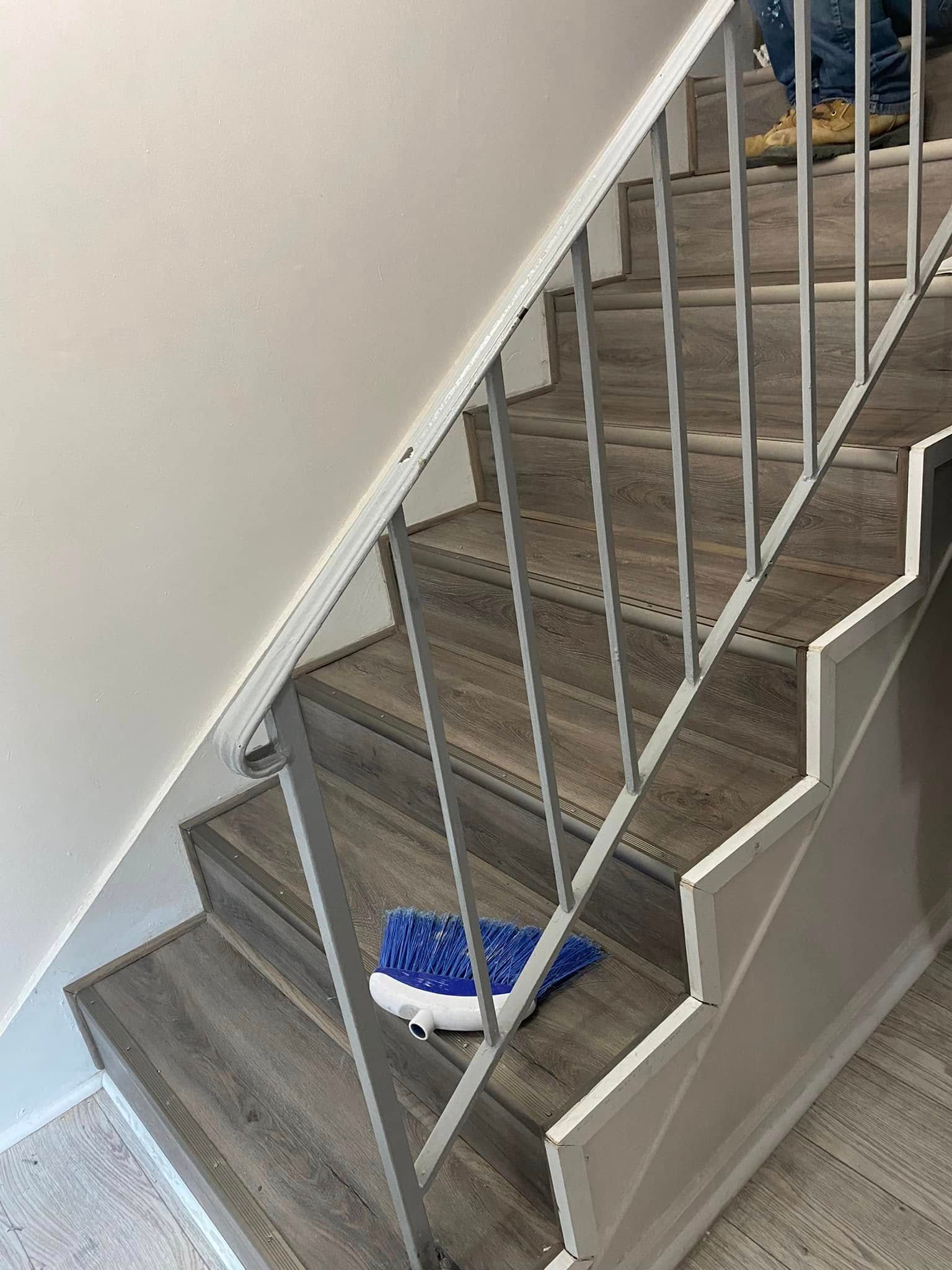 Blue sneaker on a stairway landing beside gray carpeted stairs and white railing