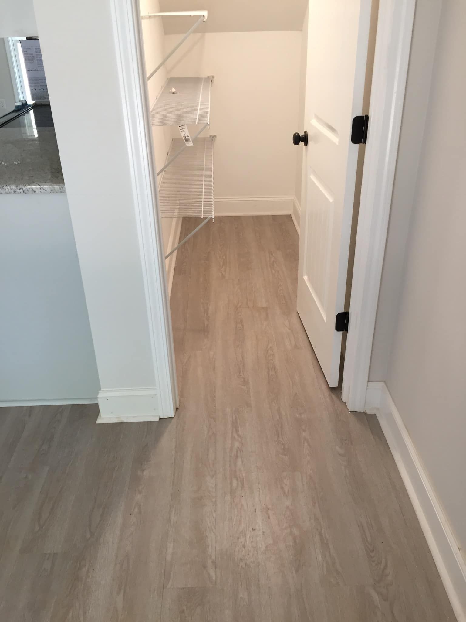 Hallway with light wood flooring leading to a white staircase and doorways, viewed from an open doorway
