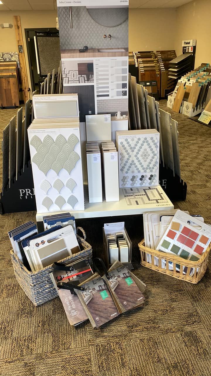Floor display of patterned wallpaper, fabric samples, and decor swatches in woven baskets.