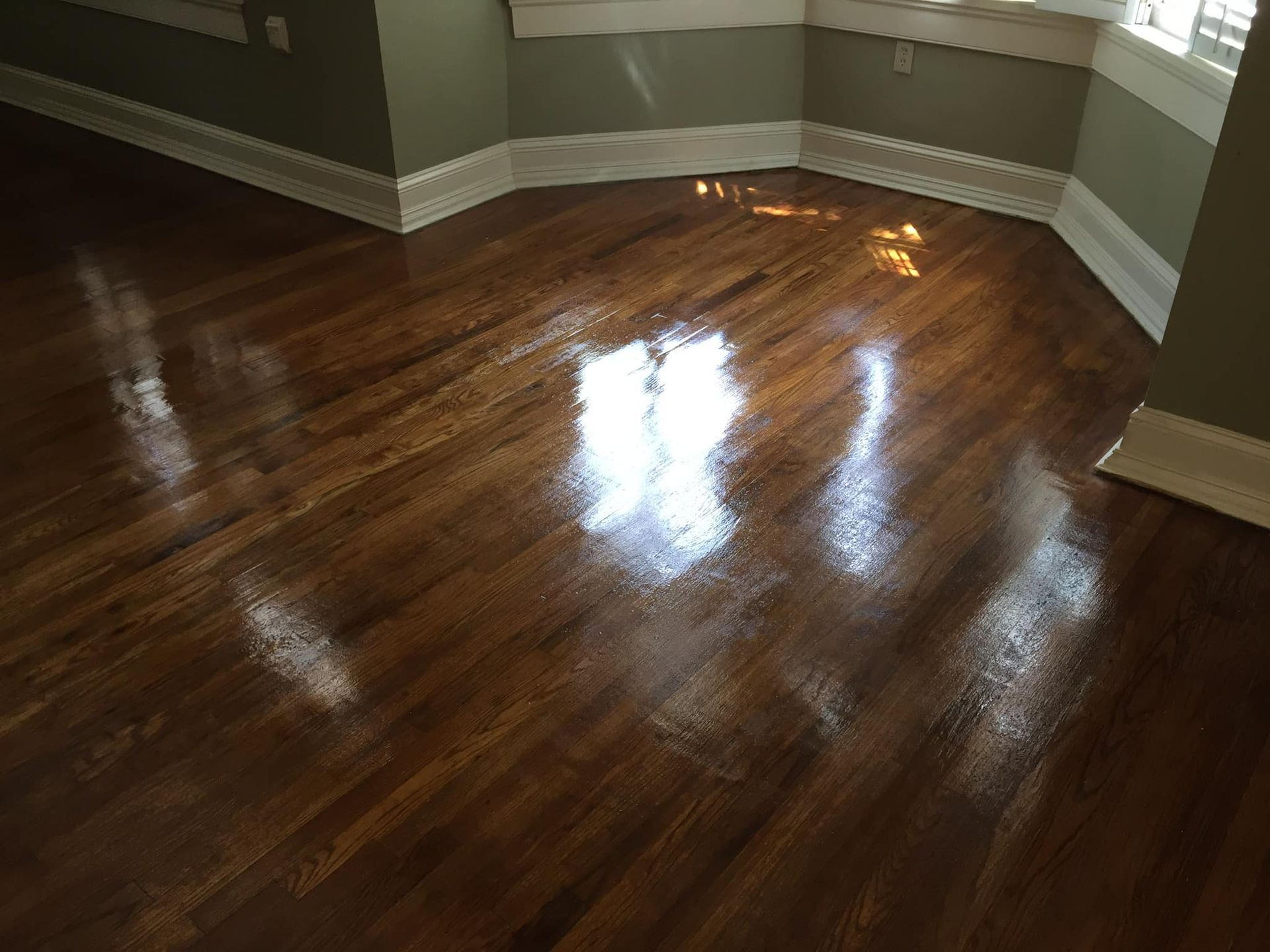 Empty room with glossy hardwood floors and gray walls lit by sunlight.