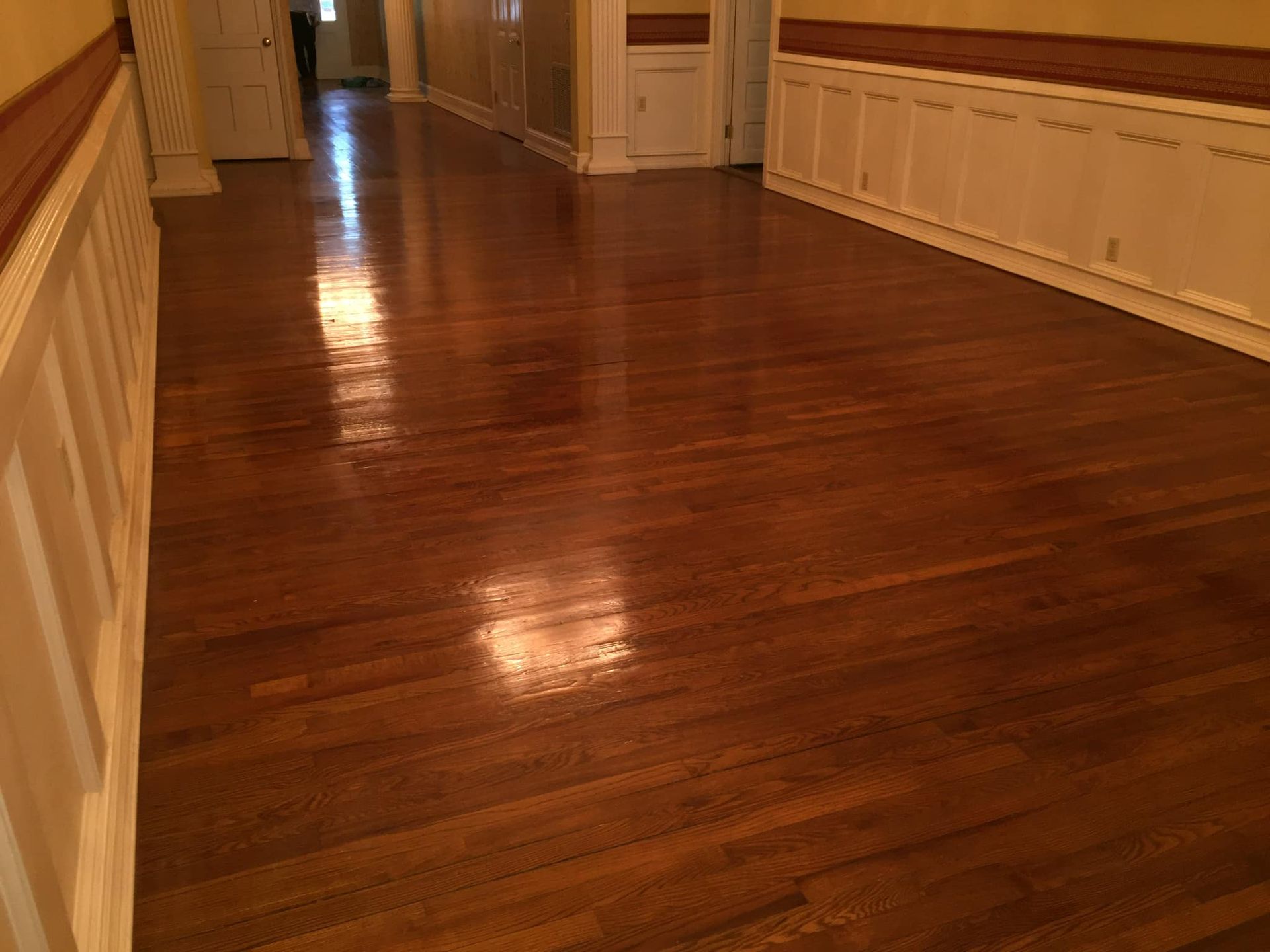 Polished hardwood hallway with white paneled walls and warm lighting