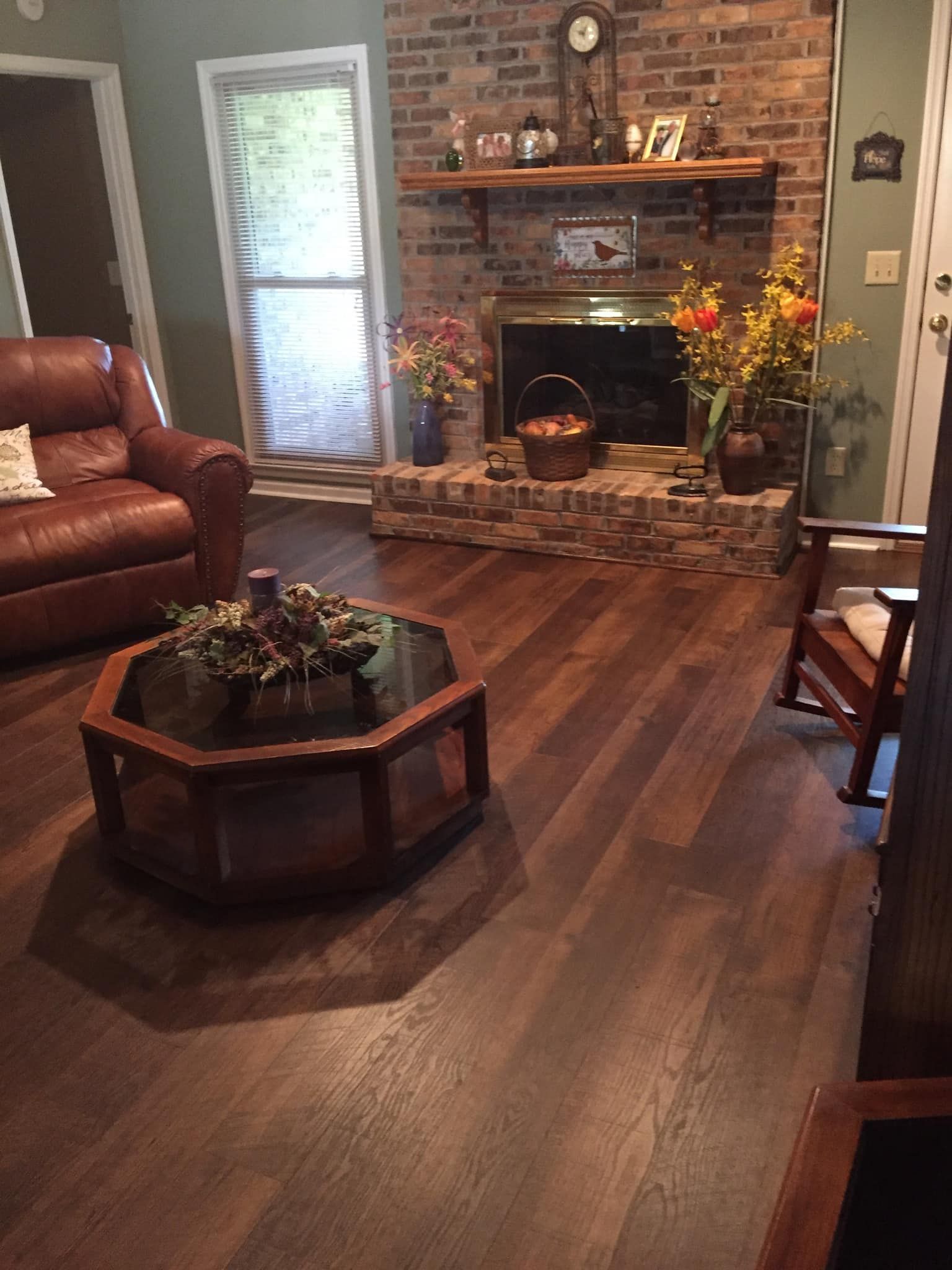 Cozy living room with leather sofa, brick fireplace, hardwood floors, and an octagonal coffee table.