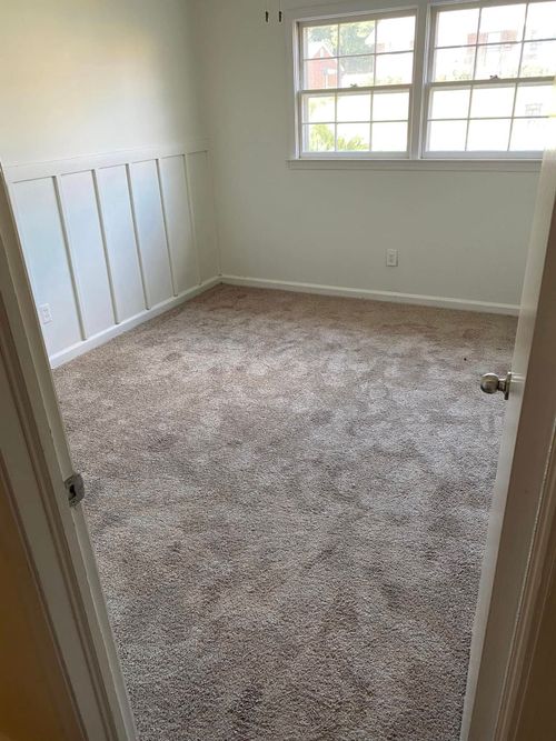 Empty carpeted bedroom with white walls, a window, and built-in closet doors.