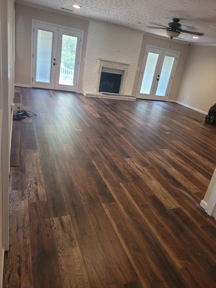 Empty living room with wood floors, white brick fireplace, ceiling fan, and glass doors.