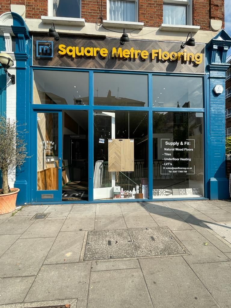 Square Meter Flooring storefront with blue trim, glass windows, and a tiled sidewalk.