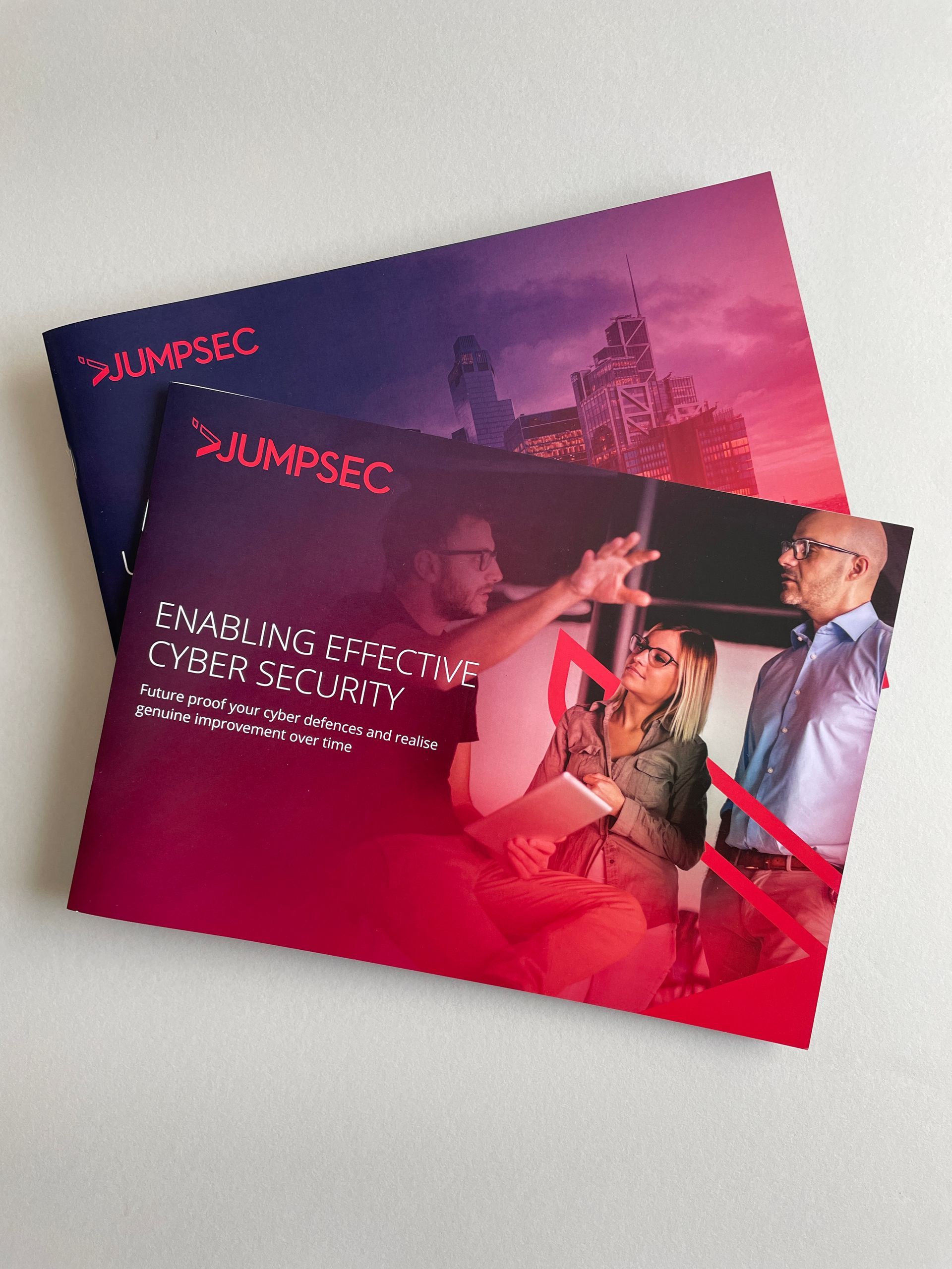 Two brochures with the Jumpsec logo. The lower brochure has a group of people, text about cyber security.