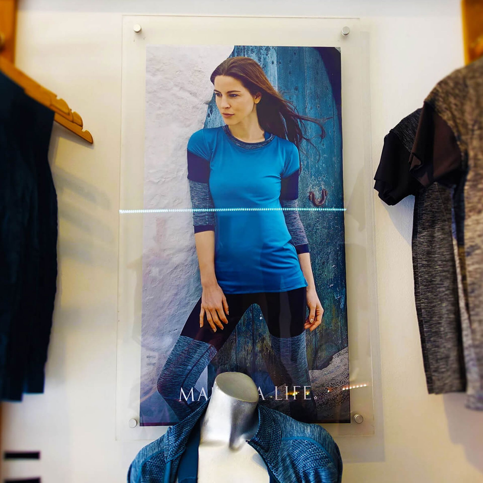 Woman wearing athletic clothing in a store display, standing in front of a rock backdrop, near clothing racks.