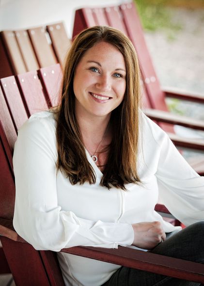 A woman in a white shirt is sitting in a red chair and smiling.