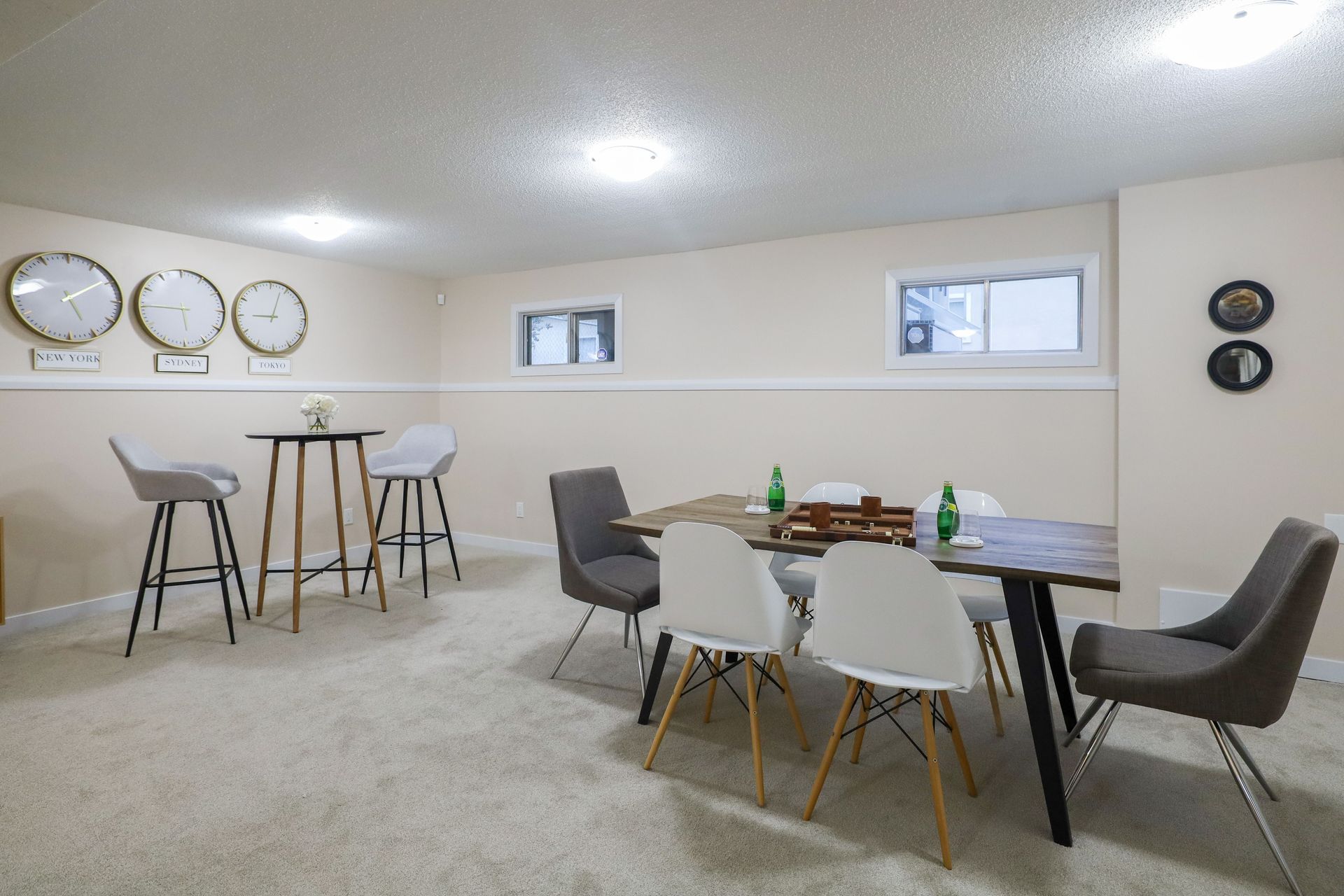 Bright dining room with black chairs, white table, bar stools, wall clocks, and windows.