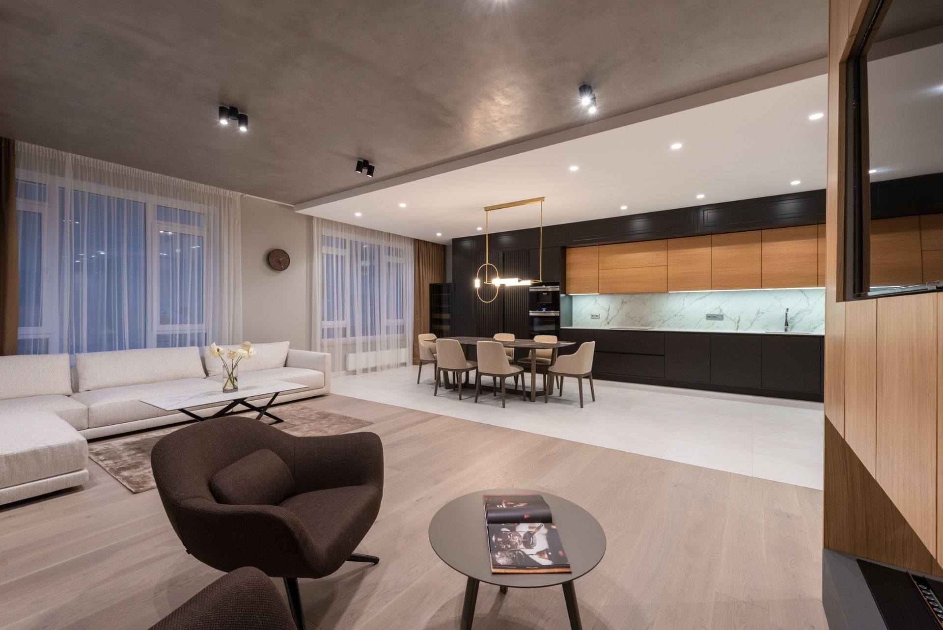 Modern open-plan living room with brown chair, white sofa, dining table, and sleek kitchen