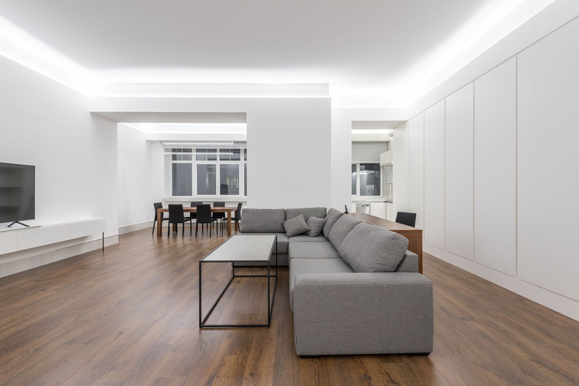Modern open-plan living room with gray sectional sofa, wood floor, and white walls.