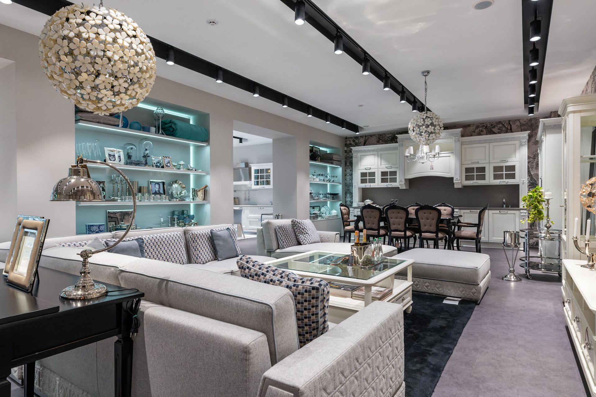 Modern living room with gray sofas, glass coffee table, teal shelves, and a dining area under pendant lights