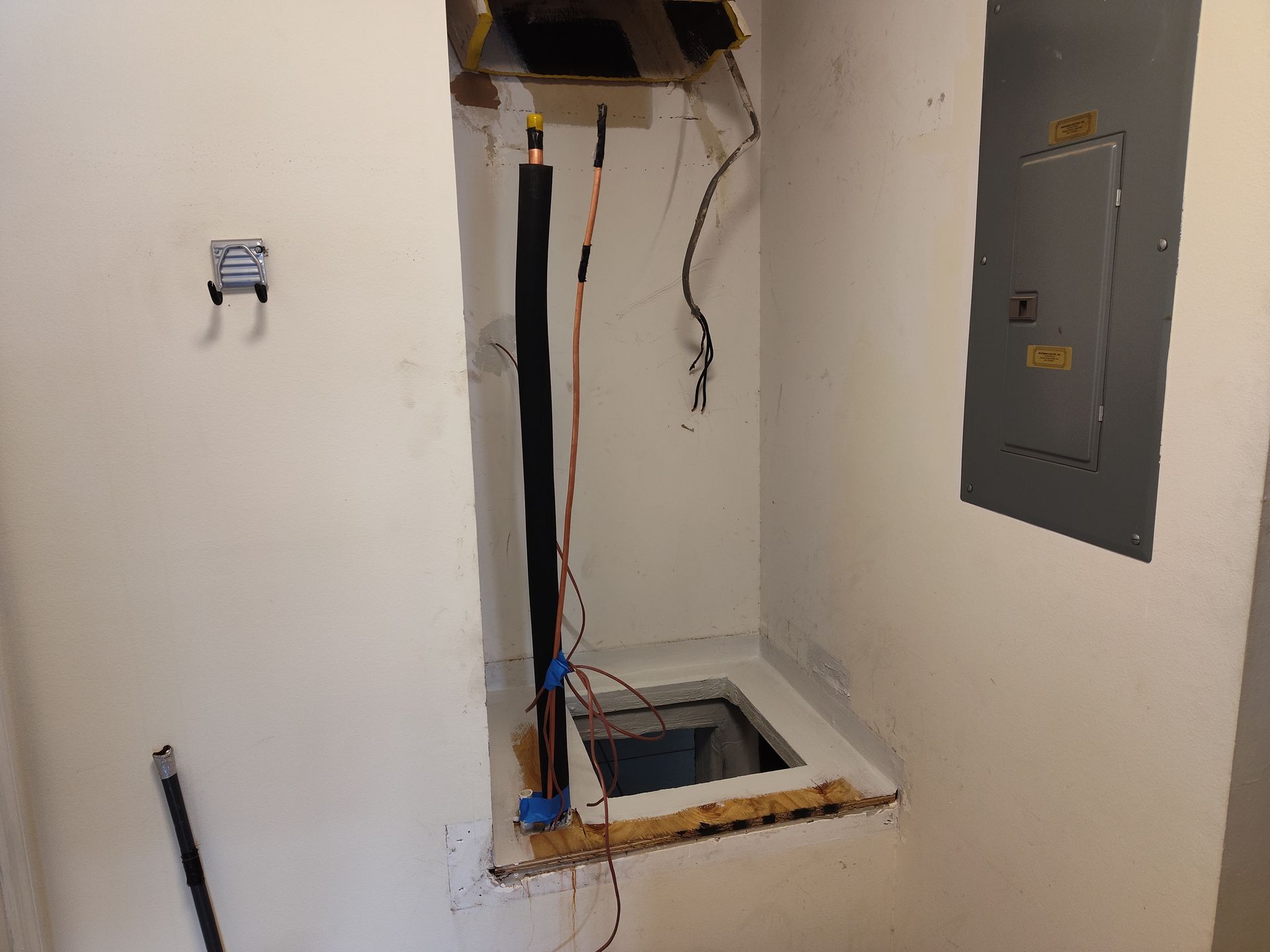 a room with a hole in the wall and wires coming out of it .
