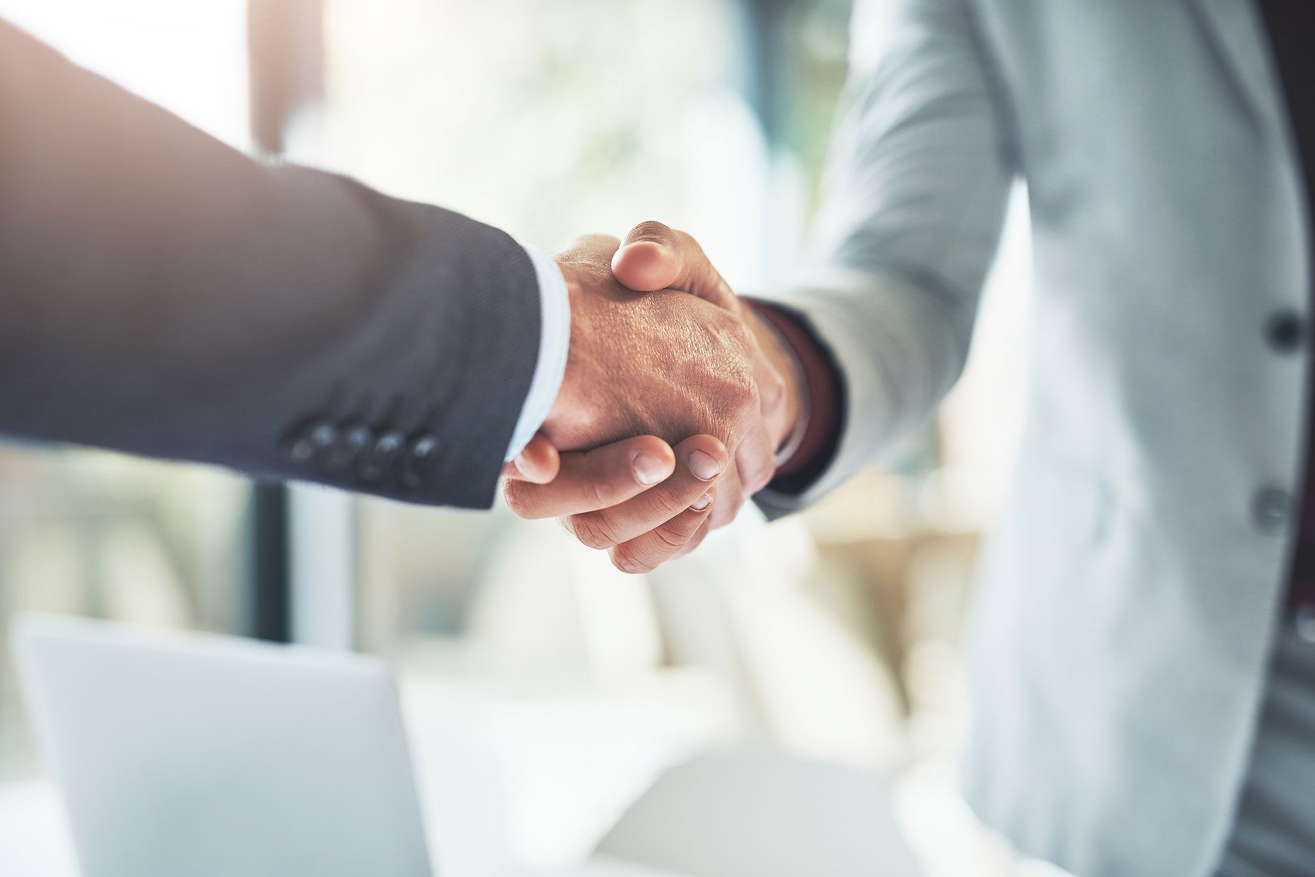 Two people in suits shaking hands indoors, as a sign of agreement.