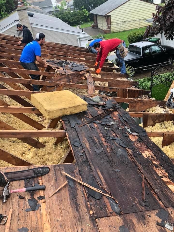 Workers repairing a damaged roof with exposed wood and tarp in a residential neighborhood