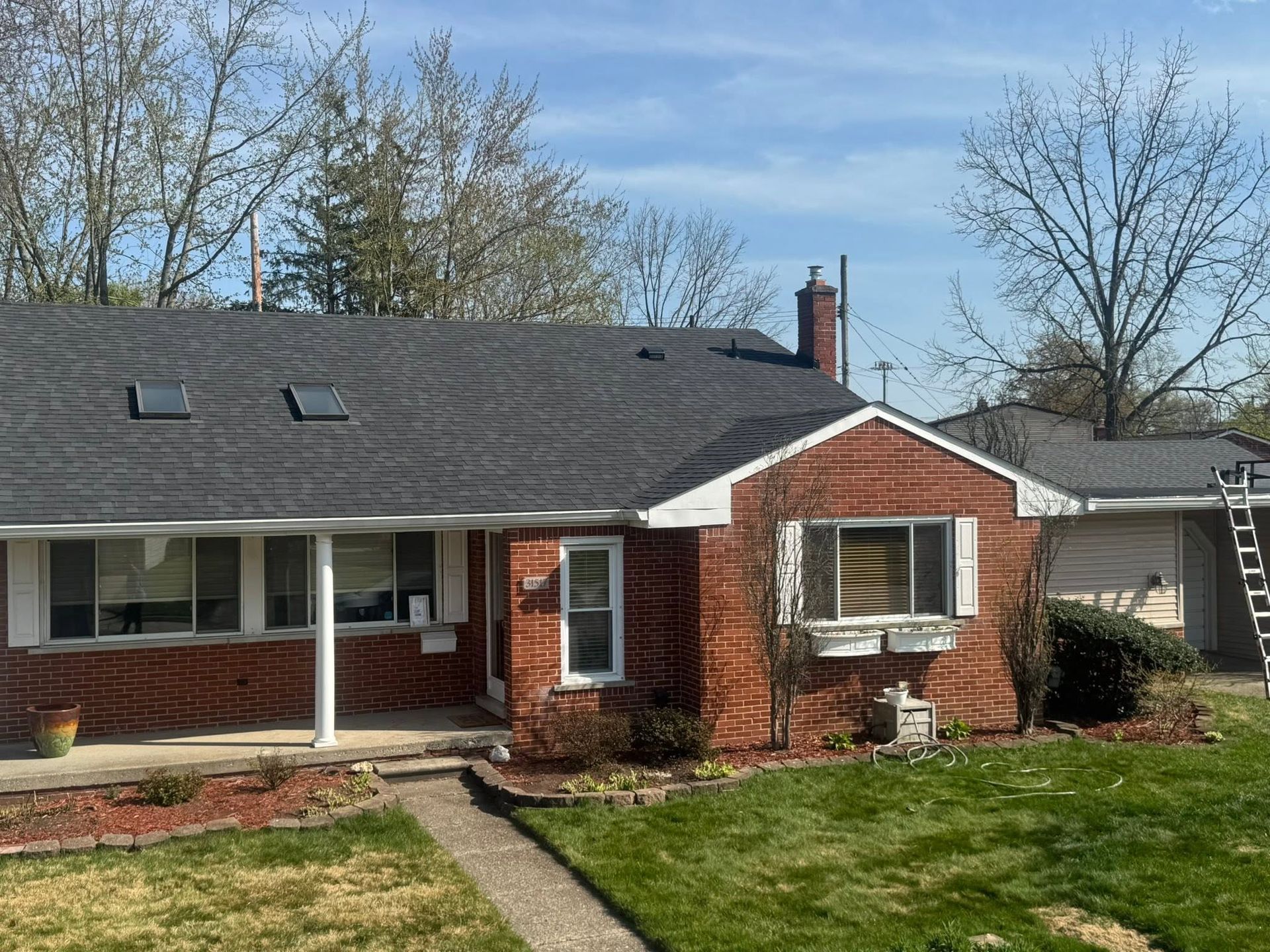 Brick ranch house with dark roof, red front door, and a green lawn under a blue sky