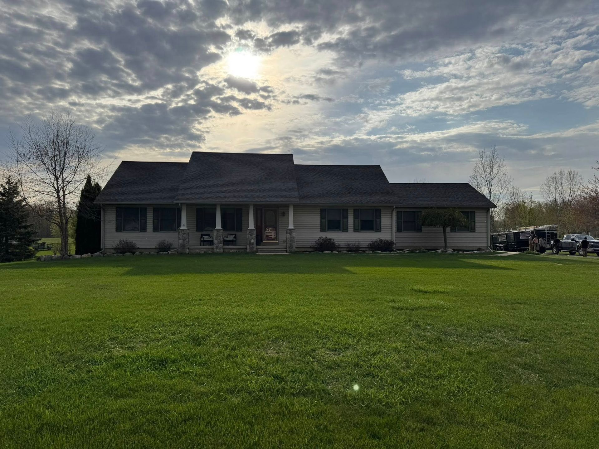 Single-story house with a gray roof and large green lawn under a cloudy evening sky.