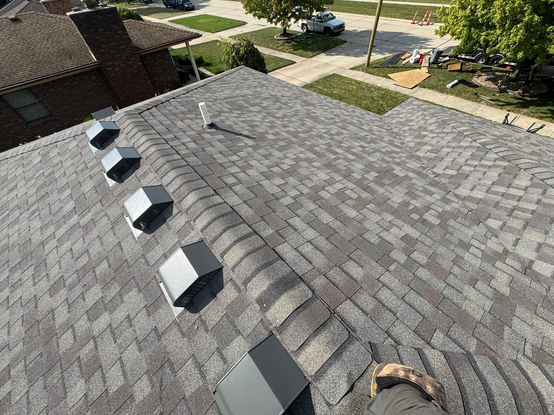 Roofing shingles with several attic vents on a gray shingle rooftop near a suburban street.