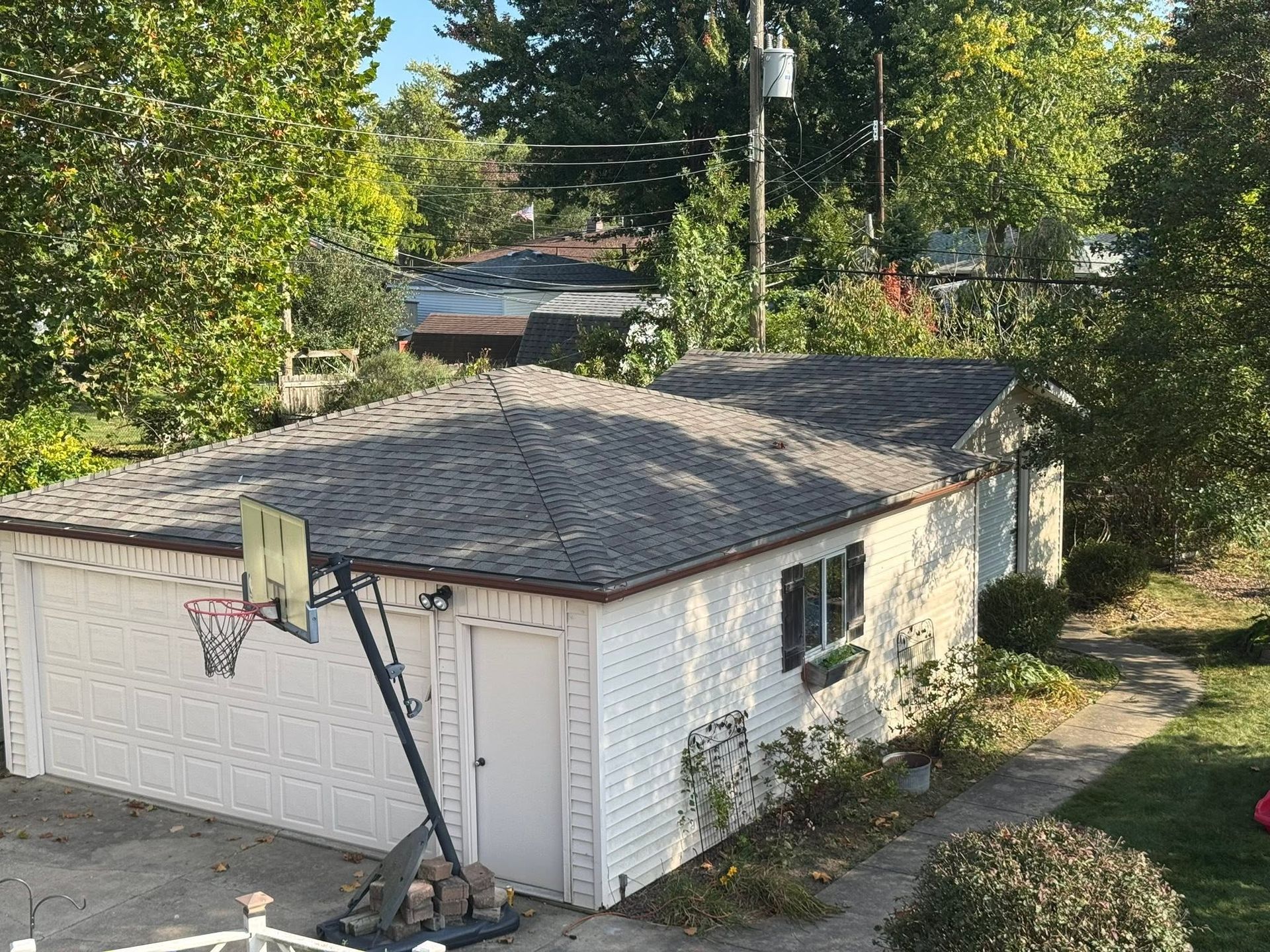 White garage with a basketball hoop, seen from above amid trees and a driveway.