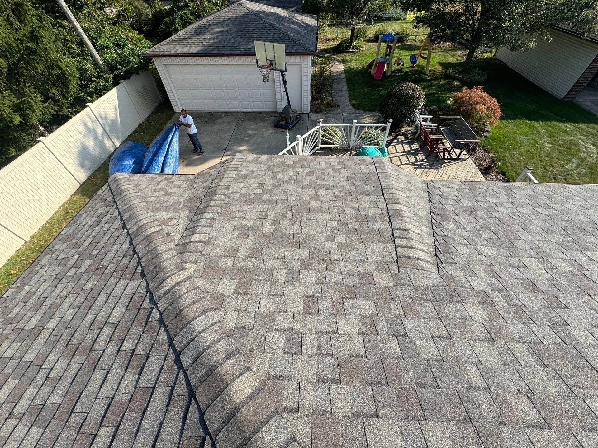 Aerial view of a gray shingled roof, detached garage, and backyard patio with plants and lawn.