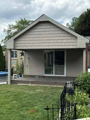 Small gray house with a front porch, sliding glass door, and a green lawn in front