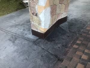 Stone pillar on a wet concrete walkway beside brick paving.