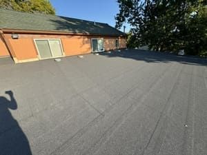 Rooftop with gray roofing, brick building wall, and trees in the background