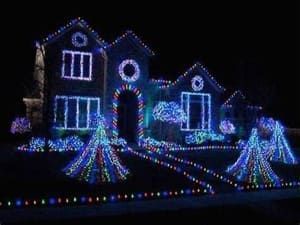House outlined in blue, purple, and white holiday lights at night, with lit trees in the yard.