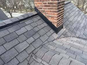 Close-up of a brick chimney on a gray shingled roof with intersecting rooflines