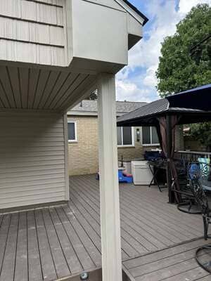 Backyard patio with gray deck, white posts, beige house, and a black umbrella over outdoor furniture.