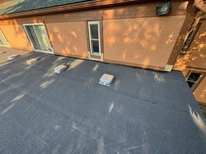Flat roof with dark roofing, skylight, and tan exterior wall with windows and vent.