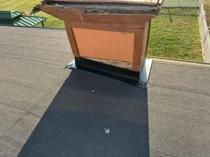 Flat black roof with a brick chimney vent and surrounding green lawn.