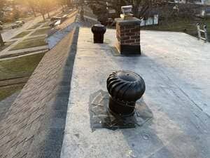 Rooftop with black metal vents and brick chimneys at sunset