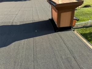 Rooftop view with dark shingles and a tan chimney vent casting a long shadow in sunlight