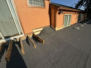 Rooftop walkway beside an orange building with windows, doors, and roof vents under bright sunlight