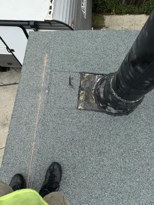 Rooftop with gray gravel surface, black vent pipe, and a person’s shoes at the edge of the frame