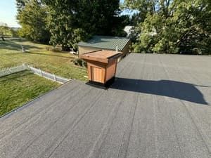 Rooftop with a small wooden vent box on gray shingles, overlooking trees and a grassy yard