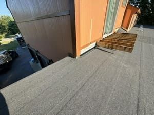Rooftop walkway beside an orange building, with a wooden ramp and dark gray roofing.