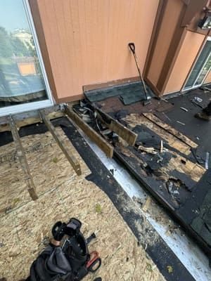 Charred rooftop debris and damaged decking beside a tan building and windows