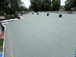 Flat gray roof under construction with vent pipes and trees in the background
