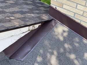 Roof valley with asphalt shingles and a brown metal flashing strip at the corner of a house.