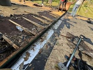 Burned wooden structure with charred debris and hoses on the ground, people standing nearby