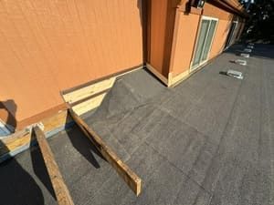 Rooftop with gray shingles, orange wall, and a small wooden ramp beside a door