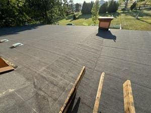 Flat roof under repair with wooden planks, trees in the background, and a chimney.