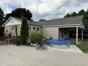 Single-story beige house with a small blue above-ground pool in the driveway under cloudy skies