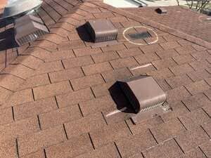 Rooftop with several brown vent boxes and a circular roof opening on shingled surface